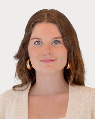 Young woman with long brown hair and large earrings, wearing a light sweater and looking directly at the camera.